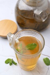 Aromatic mint tea and fresh leaves on white textured table, closeup