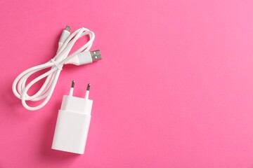 USB power adapter and charge cable on pink background, flat lay. Space for text