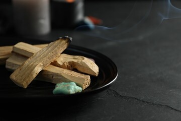 Smoldering palo santo stick and gemstone on black table, closeup. Space for text