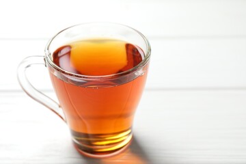 Aromatic black tea in cup on white wooden table, closeup. Space for text