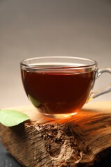 Aromatic black tea in cup and green leaf on wooden snag, closeup