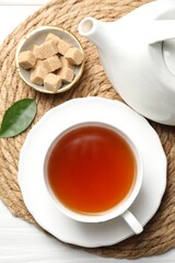 Aromatic black tea and brown sugar cubes on white wooden table, top view
