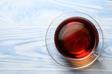 Aromatic black tea in cup on light blue wooden table, top view. Space for text