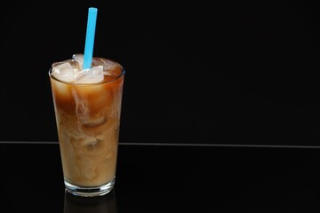 Refreshing iced coffee with milk in glass on black mirror surface. Space for text