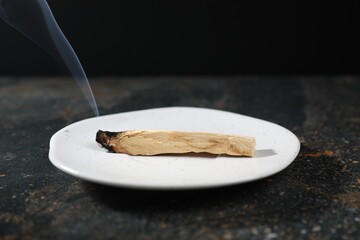 Smoldering palo santo stick on dark table, closeup
