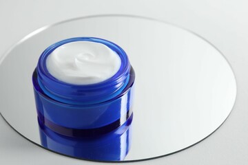 Jar of cream and mirror on light background, closeup. Space for text