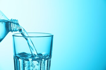 Pouring soda water from bottle into glass on light blue background, closeup. Space for text