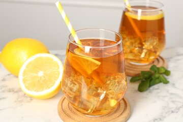 Refreshing iced tea with slices of lemon and drinking straws on white marble table, closeup