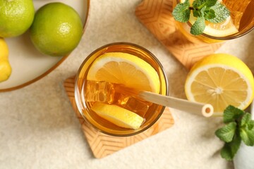 Refreshing iced tea with drinking straw, mint, lemon and lime on light textured table, flat lay