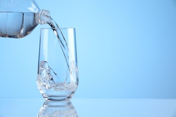 Pouring refreshing soda water from bottle into glass on light blue background, closeup. Space for text