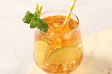 Refreshing iced tea with slices of lime, mint and drinking straw in glass on light table, closeup