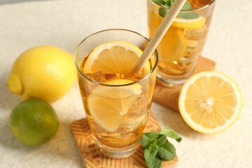 Refreshing iced tea with drinking straw, mint, lemon and lime on light textured table, closeup