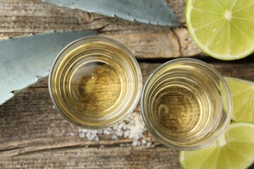 Mexican tequila shots, slices of lime, salt and agave leaves on wooden table, flat lay