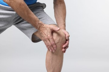 Senior man suffering from knee pain on light grey background, closeup. Space for text