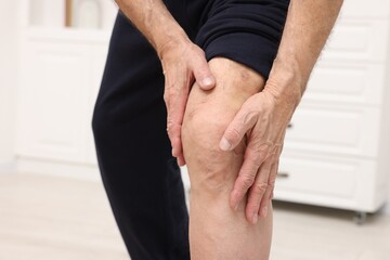 Senior man suffering from pain in his knee indoors, closeup