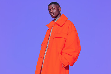 Stylish young person in a bright orange oversized jacket against a solid purple background