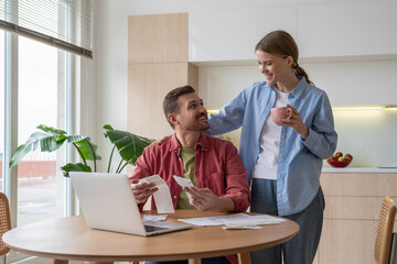 Happy family couple calculate expenses using online banking service on laptop at cozy home. Loving...
