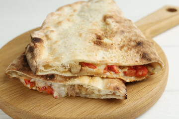 Halves of tasty calzone with meat, cheese and tomato on white wooden table, closeup