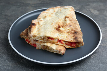 Halves of tasty calzone with meat, cheese and tomato on grey textured table, closeup
