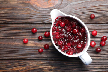 Tasty cranberry sauce in gravy boat and berries on wooden table, top view