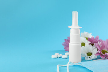 Allergy treatment. Nasal spray, pills, protective mask and flowers on light blue background. Space for text