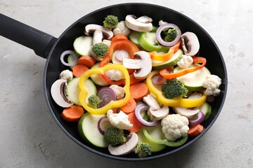 Frying pan with mix of vegetables and mushrooms on light grey table, above view