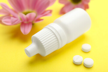 Allergy treatment. Nasal drops, pills and flowers on yellow background, closeup