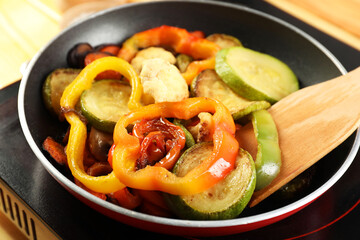 Frying pan with vegetables and stove on table, closeup