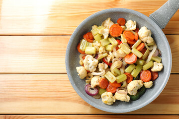 Frying pan with vegetables on wooden table, top view. Space for text