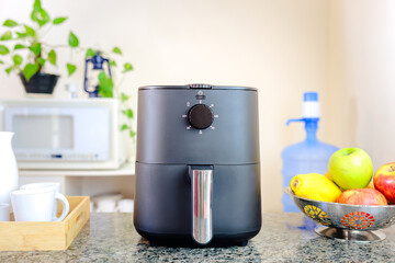 Black air fryer on a kitchen countertop in a cozy Brazilian home. A modern appliance for healthy cooking, surrounded by fresh fruits, a microwave, and a water dispenser in the background