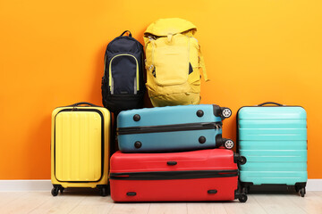 Many colorful suitcases and backpacks on floor near orange wall