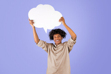 Positive african american teenager holding empty speech bubble above his head over blue background,...