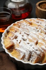 Delicious bread pudding with raisins, powdered sugar and tea on table, closeup