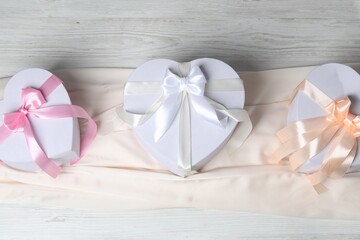 Beautiful wedding gifts and silk fabric on light wooden table, flat lay