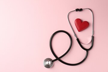 Fototapeta premium Cardiology. Stethoscope and red decorative heart on pale pink background, flat lay. Space for text