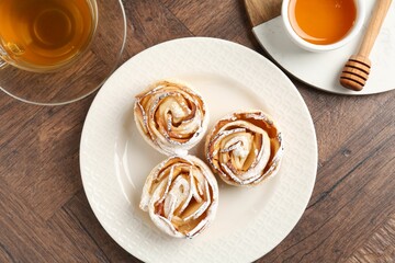 Freshly baked apple roses, honey and tea on wooden table, flat lay