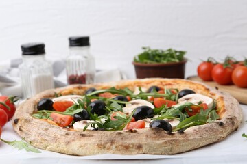 Tasty pizza with cherry tomatoes, black olives, mushrooms and arugula on white table, closeup
