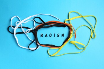 Word Racism and shoelaces of different colors on light blue background, top view