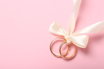 Wedding rings tied with ribbon on pink background, top view