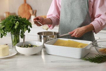Woman making spinach lasagna at marble table indoors, closeup