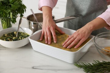 Woman making spinach lasagna at marble table indoors, closeup