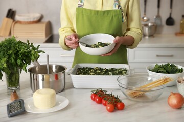 Woman making spinach lasagna at marble table in kitchen, closeup