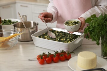 Woman making spinach lasagna at marble table indoors, closeup