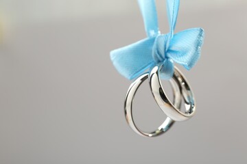Silver wedding rings tied with ribbon on light grey background, closeup. Space for text