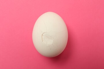 One egg with cracked shell on pink background, top view