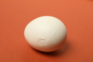 One egg with cracked shell on red background, closeup