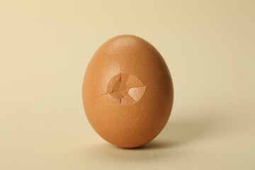 One egg with cracked shell on beige background, closeup