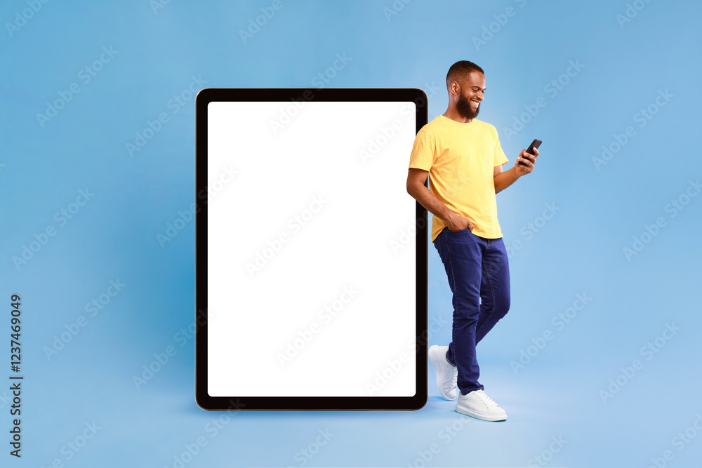 Poster optimistic young african american man leaning on huge tablet computer with blank white screen, using