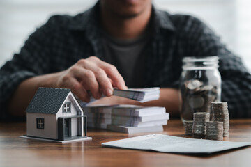 Man organizes cash with coins, a contract, and a miniature house, symbolizing financial management,...