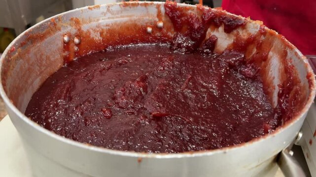 Close-up view of the hand of a white color skin pastry chef preparing homemade quince jelly in her traditional workshop in a big pot. 4K